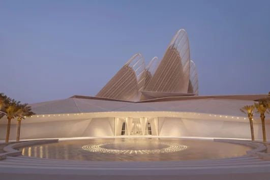 Front entrance of the Zayed National Museum at dusk with soft lighting and falcon-wing towers in the background