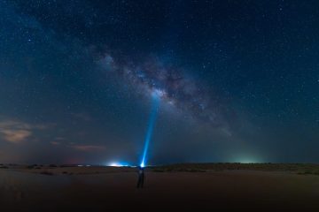 Milky Way galaxy visible over UAE desert dunes during night stargazing experience with light beam pointing to the sky