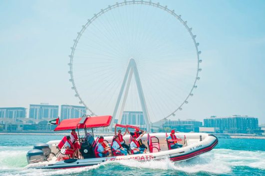 Tourists enjoying a high-speed boat ride with Ain Dubai Ferris wheel visible in the background in Dubai Marina.