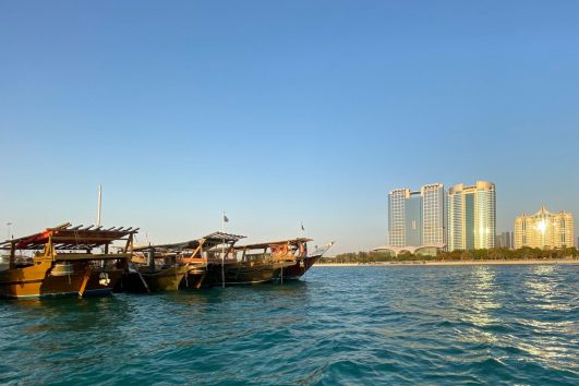 Traditional wooden dhow boats docked on calm waters with modern Abu Dhabi skyline in the background during sunset