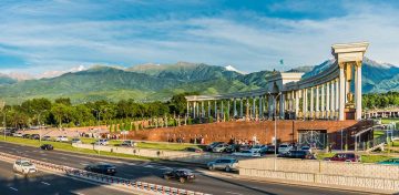 Panfilov Park in Almaty with colonnades, city traffic, and Tian Shan mountains in the background