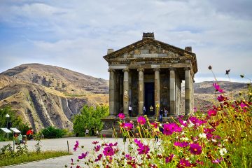 Garni Temple in Armenia with pink flowers in the foreground and mountains in the background