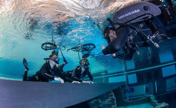 An instructor gives a thumbs-up to two student divers practicing buoyancy near the surface of the pool.