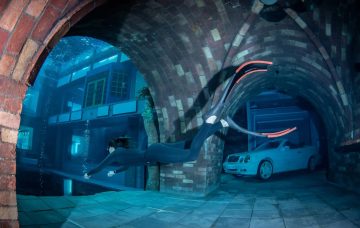 A freediver swims through a brick archway toward a white convertible car submerged in Deep Dive Dubai.