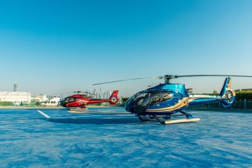 Blue and red Falcon helicopters parked on a helipad with Dubai skyline in the background