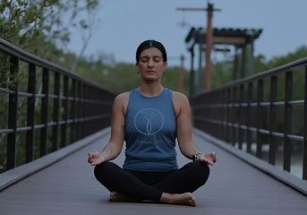 Woman meditating in lotus pose on boardwalk during evening