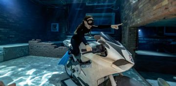 A freediver posing on a white Ducati motorcycle submerged within the brick-walled sunken city.