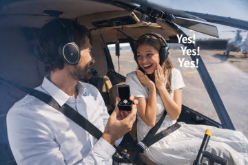 Man proposing with diamond ring inside helicopter as woman reacts with joy
