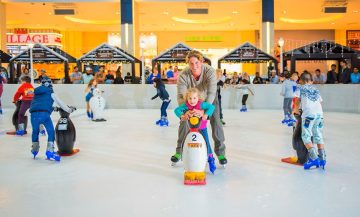 father helping child ice skating with penguin aid Dubai Ice Rink Dubai Mall