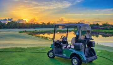 golf cart parked near lake on golf course during sunset