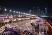 Elegant rooftop dining area on a dhow cruise with Dubai Marina skyline at night.