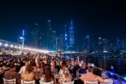 Guests enjoying dinner on the upper deck with the illuminated Dubai Marina in the background.