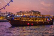 Traditional wooden dhow cruise reflecting on the waters of Dubai Marina at night.