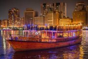 Traditional Dhow Cruise with Dubai’s skyline in the background at night.