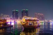 raditional dhow boat, illuminated with string lights, cruising on Dubai Creek at night.