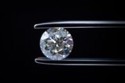 Diamond held by tweezers against a dark background