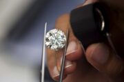 Close-up of a jeweler inspecting a round-cut diamond with tweezers and a loupe