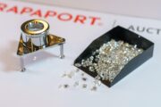 Magnifying loupe and tray of polished diamonds on a white background with RAPAPORT branding in the background