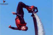 A fly boarder in a red vest executing a mid-air flip over the ocean