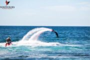 A Fly Boarder propelled into a high arc over the ocean, leaving a trail of water spray.