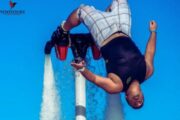 A fly boarder performing an upside-down aerial stunt against a clear blue sky.