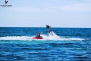 A fly boarder soaring over the ocean while being supported by a jetski.