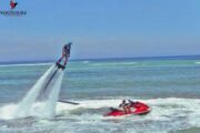 A fly boarder propelled high into the air by water jets, with a red jetski below.