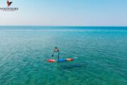 A paddleboarder on a colorful board gliding across clear, turquoise waters.