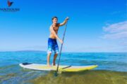 A man paddleboarding on calm, turquoise waters under a bright blue sky.