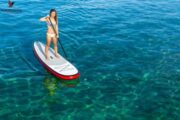 A woman paddleboarding confidently in crystal-clear water.