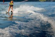 A woman confidently water skiing, creating a splash as she glides over the wake.