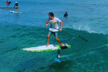 A rider balancing on an e-Foil board, riding the waves with a paddle in hand.