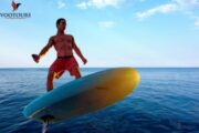 A man riding an e-Foil board, balancing effortlessly over calm ocean waters at sunset