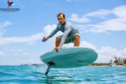 A man mid-action while riding an e-Foil board over clear blue waters.