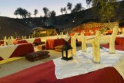 Elegant table setup with traditional seating in a desert camp at dusk.