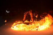 Performer surrounded by flames during a fire dance show at a desert camp.