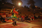 Tanoura dancer spinning in a vibrant, multicolored costume during a desert camp show.