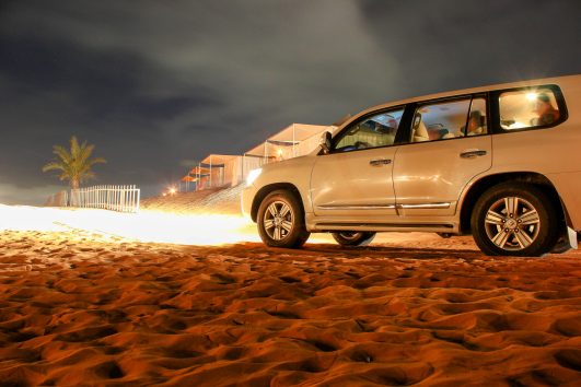 4x4 vehicle parked on sand dunes in a desert camp at night