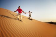 Two men enjoying sandboarding on golden dunes in the desert