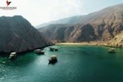 Multiple dhow boats in a calm bay surrounded by rugged hills.