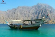 Traditional dhow floating on crystal-clear water against a rocky mountain backdrop