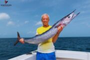 Elderly man proudly holding a large fish caught during deep-sea fishing.