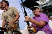 A woman enjoying deep-sea fishing with excitement, holding a fishing rod while surrounded by a crew.