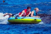 Couple laughing on a donut ride over the waves.