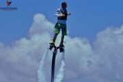 A person standing tall on a FlyBoard above the ocean, surrounded by white water sprays.