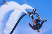 A person performing an upside-down flip on a FlyBoard against a clear blue sky.