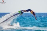 A person diving forward from a FlyBoard above the ocean waves.