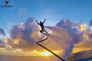 A person soaring high on a FlyBoard at sunset, creating a silhouette against vibrant clouds.