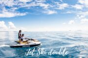 A couple riding a jet ski on calm, turquoise waters under a beautiful blue sky.