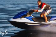 Man riding a blue and white jet ski, creating a splash on calm waters in Ras Al Khaimah.